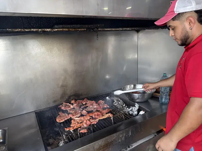 Parrillero volteando carne sobre la parrilla de carbón