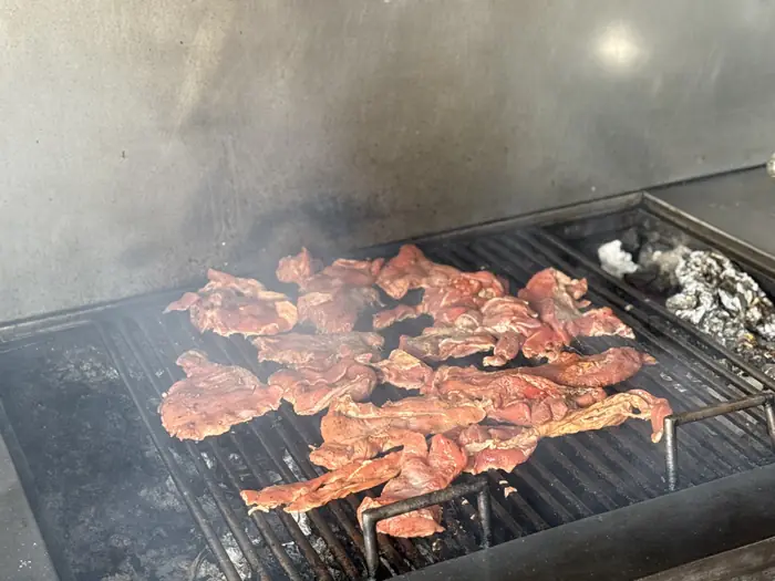 Carne extendida sobre la parrilla entre humo